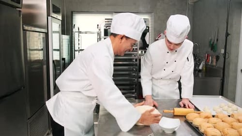 Asian male chefs in uniforms are preparing to bake bread in a stainless kitchen.