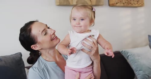 Caucasian mother smiling while holding her baby sitting on the couch at home
