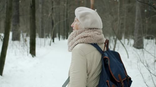 Cheerful Senior Woman in Warm Clothes Walking in Park Looking Around Enjoying View in Winter