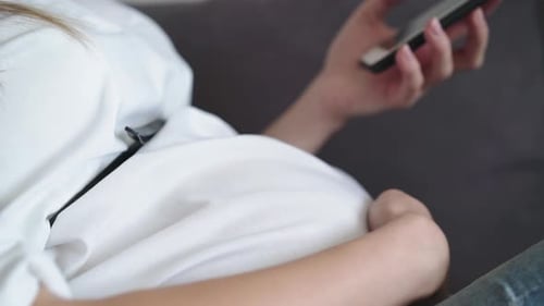 Pregnant Woman Relaxes and Uses Smartphone Indoors