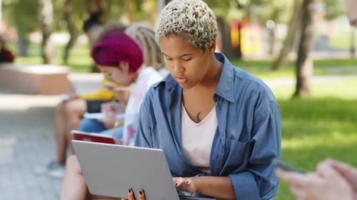 Cheerful Mixed-Race Female Student Using Laptop and Posing for Camera in Park