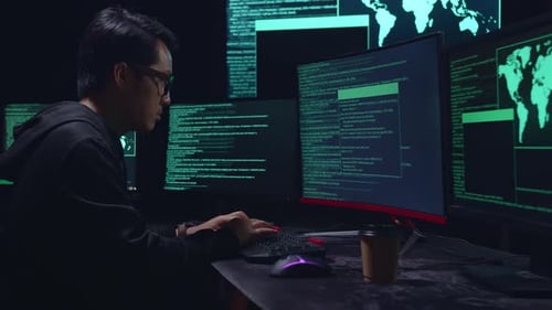 Asian Male Hacker Hacking With Multiple Computer Screens In Dark Room
