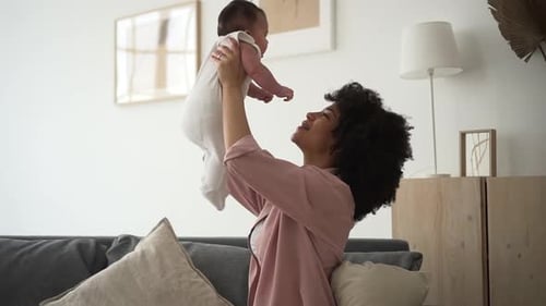 Mama spielt mit kleiner Tochter und küsst sie, während sie auf der Couch im Apartment Room sitzt Spbd