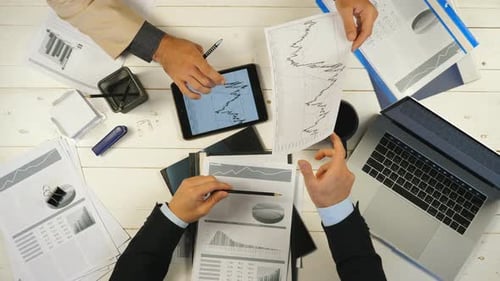 Male Hands of Two Successful Business Partners Examining Graphs and Discussing Financial Reports in