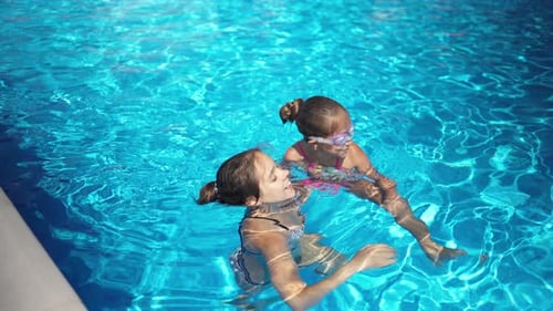 Zwei Mädchen in hellen Bikinis spielen zusammen in einem Pool mit blauem Wasser an einem Sommertag