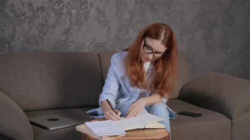 Woman Writes in Notebook on Sofa Indoors