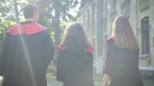 Back View Cheerful Caucasian Young Students Throwing Mortarboards in Sunshine at College Campus