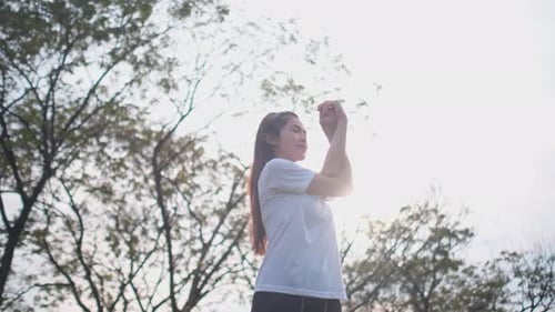 Asian sport woman warm-up with arm and body stretching in green park with sunset light
