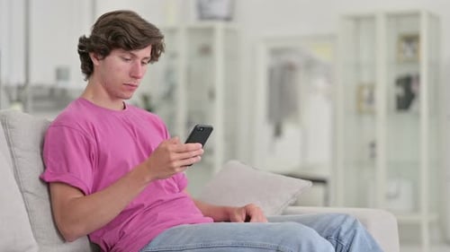 Young Adult Using Mobile Phone on Couch Indoors