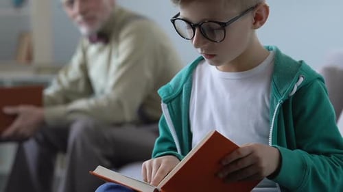 Boy Reading Book with Adult in Background
