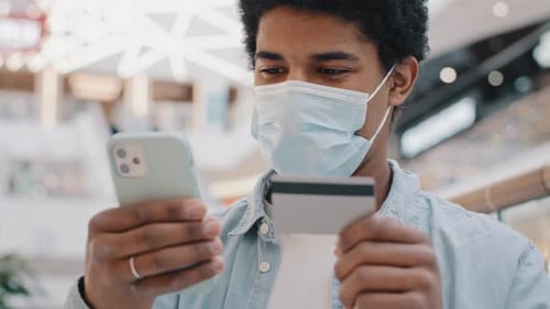 Afroamerikaner Kunde Kunde in medizinischer Maske, der Bank-Kreditkartendaten im Telefon eingibt