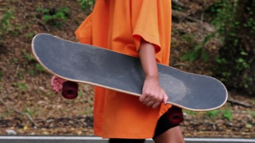 Teen Walks with Skateboard on Path