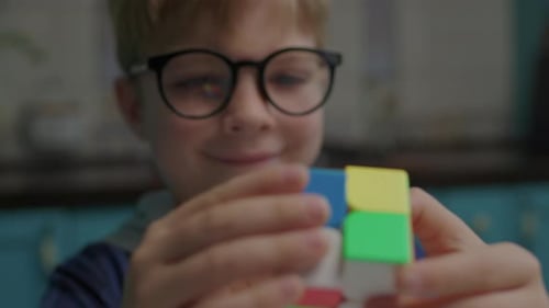 Close Up of Boy in Eye Glasses Solving Color Cube Puzzle in Hands