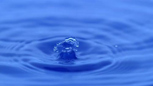 Single Drop Creates Abstract Ripples in Blue Water