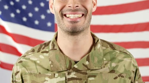 Smiling Soldier in Camouflage Uniform With Flag Backdrop