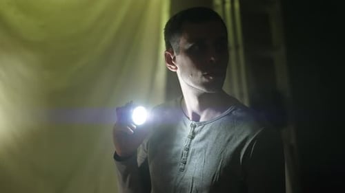 Man Holds Flashlight in Dark, Mysterious Setting