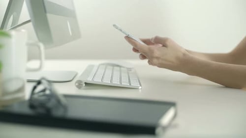 Hands Typing on Smartphone at Computer Desk