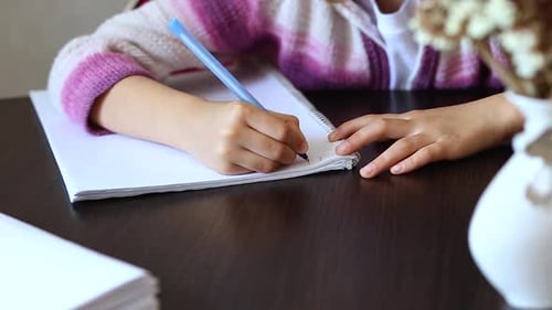 Child Writes in Notebook at Table