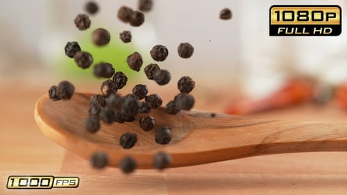 Black peppercorns falling onto a wooden spoon