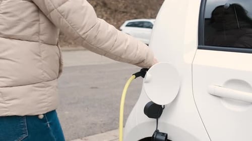 Woman Coming to the Electric Vehicle and Unplugging Power Supply Cable to Charge in the Street at