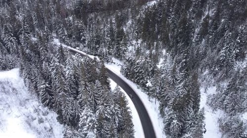 Aerial top view snowy forest mountains with cars driving winter road.