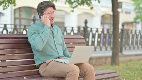 Adult Man on Phone and Laptop on Park Bench