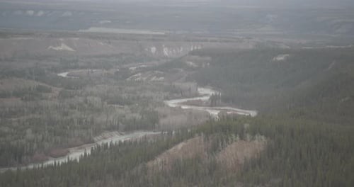 Aerial helicopter shot circling around sparsely forested hilltop, highway in distance, drone footage
