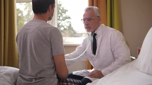 Doctor Using Stethoscope To Examine Patient in Ward