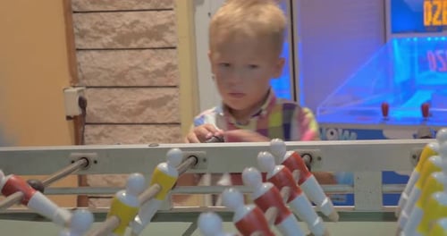 Child Plays Foosball in Brightly Lit Arcade