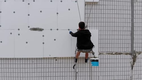 Aerial View on Industrial Climber Suspended on Ropes Performs Work on Insulation of Facade of High