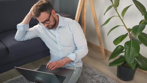 Man Using Laptop While Sitting on Rug Indoors