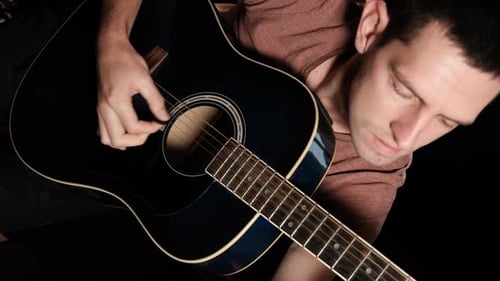 Vertikales Video. Young Man Blogger spielt eine Akustikgitarre auf schwarzem Hintergrund