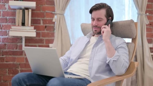 Man Sits with Laptop, Answers Phone Call