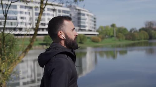 Adult Man Runs in the Park Near the City Camera Following Runner in Wireless Headphones Healthy