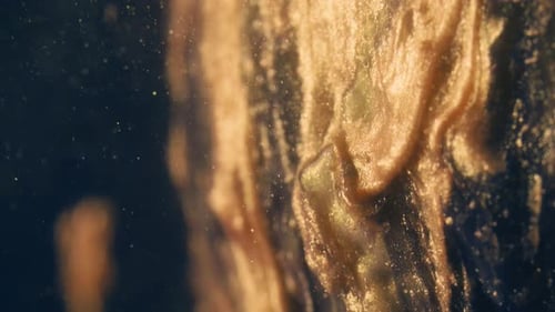 Golden Ink Particles Flows in Water As Colorful Chaos on the Black Background