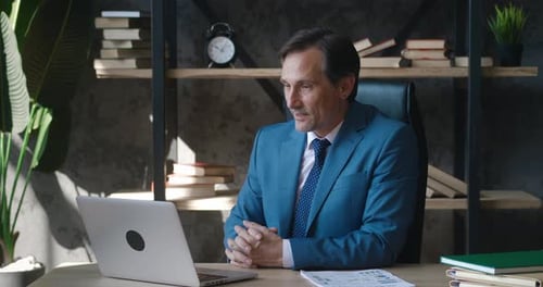 Happy Mature Male Businessman CEO Having Video Call Using Laptop Computer While Sitting at Office
