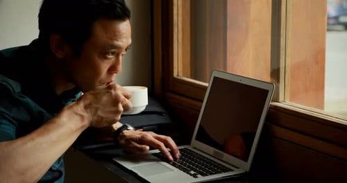 Mann trinkt Kaffee, während er Laptop benutzt