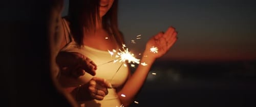 Young couple lighting up a sparkler to celebrate on the hill at sunset. Close up.