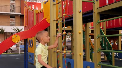 A Child Climbs a Grid in a Park on a Playground on a Hot Summer Day