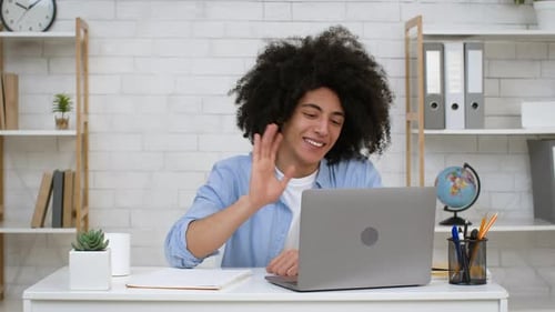 Smiling Man Video Chats at Desk Using Laptop