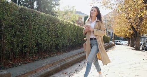 Young Attractive Business Woman Walks Around Historic Green Urban Area, with Take Away Cup and Drink