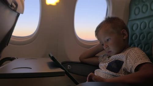 Child Using Tablet on Airplane During Sunset