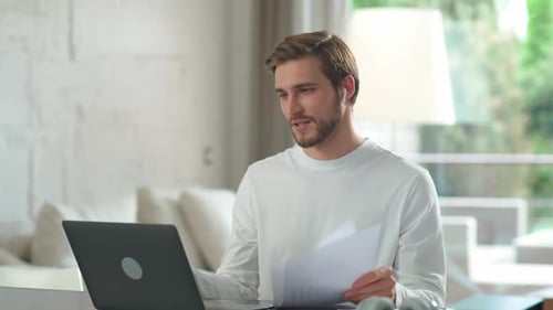 Man Video Conferencing With Documents at Desk