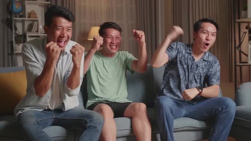Three Asian Males Cheering And Watching Football Game On Tv And Celebrating Victory At Home