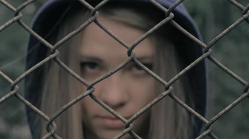 Teen Behind Fence Looks Sadly at Camera