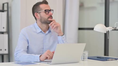 Thoughtful Man Working on Laptop in Bright Office