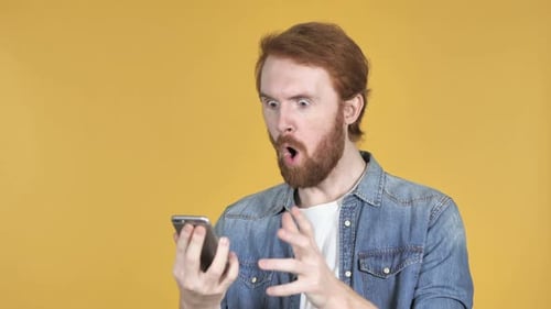 Amazed Redhead Man Surprised While Using Smartphone Yellow Background