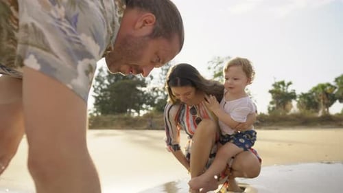4K Caucasian family parents and little baby son playing beach toy together on the beach in sunny day