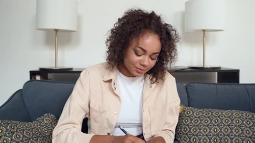 Woman Gesturing While Taking Notes on Couch