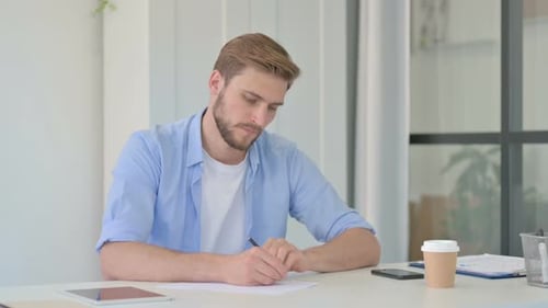 Man Writes on Paper at Desk in Office